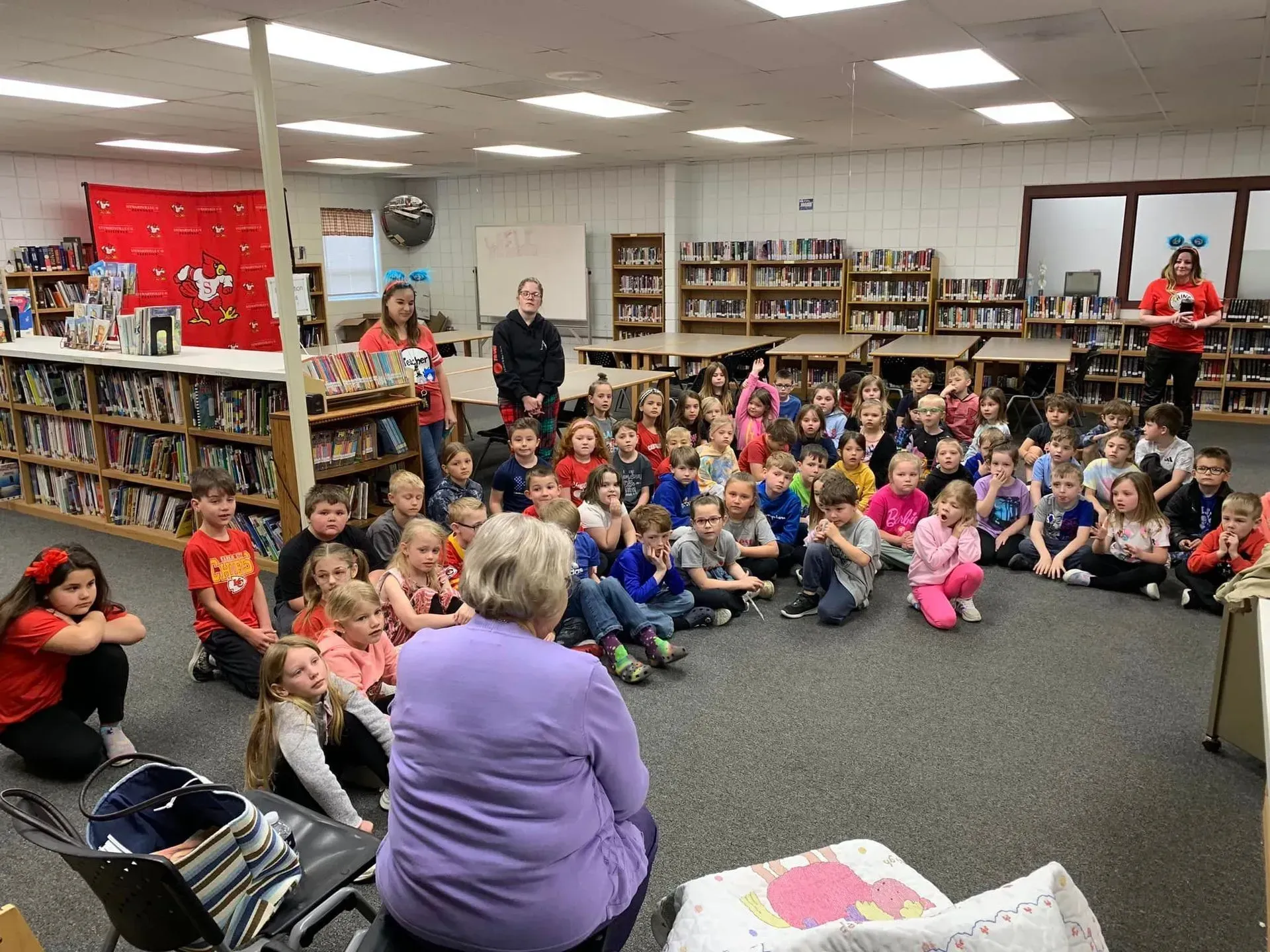 Children sitting on a library floor for a group storytime with an adult leader