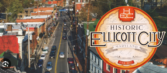 An aerial view of a main street in Historic Ellicott City, Maryland, with a circular town logo overlay.