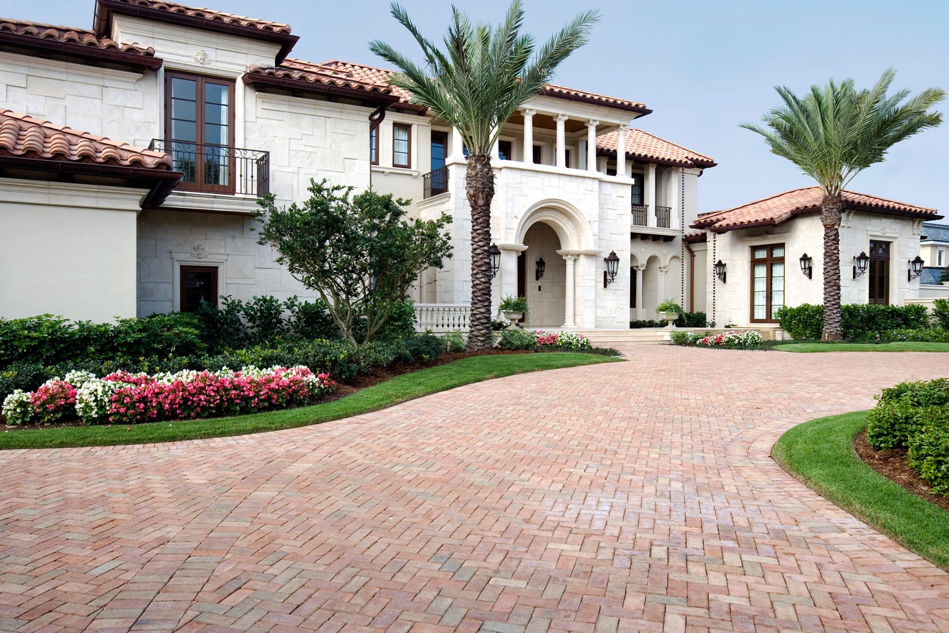 A large white house with a brick driveway and palm trees