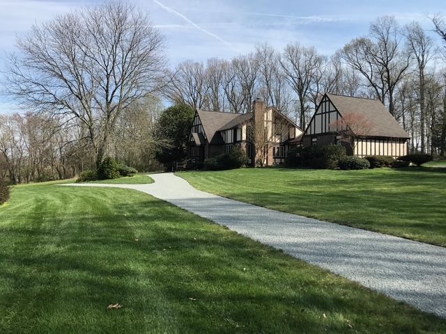 A large house with a driveway leading to it is surrounded by trees and grass.