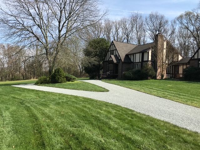 A large house with a lush green lawn and a gravel driveway leading to it.