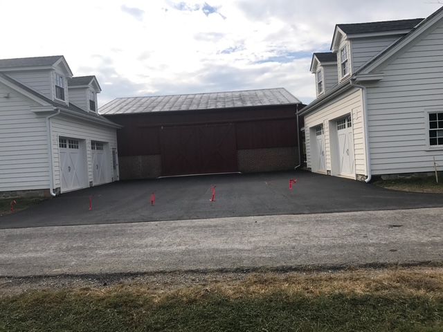 A parking lot between two white houses with a red barn in the background.