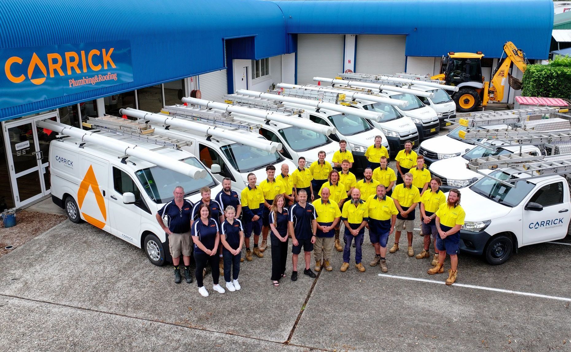 Wauchope Plumbing team stands in front of a line of company vans branded with the