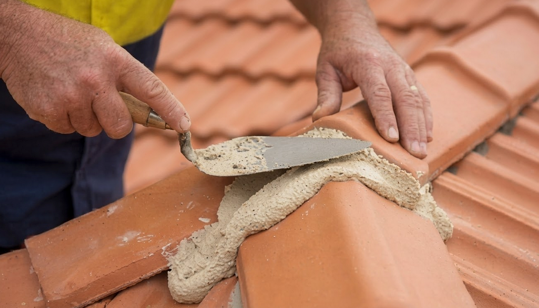 Roofer using a trowel to apply mortar on terracotta roof tiles.