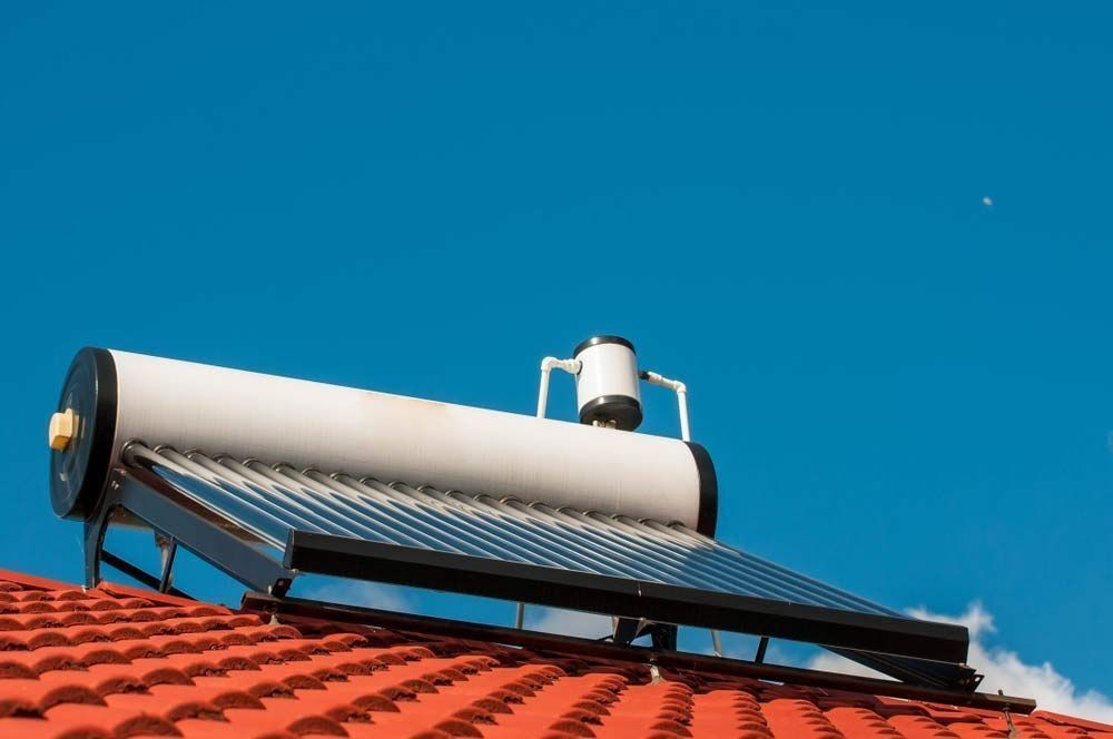 A solar hot water heater is sitting on top of a red tiled roof.