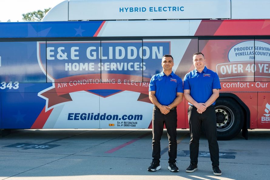 Eight E&E Gliddon employees in blue shirts pose in front of a branded hybrid electric service truck.