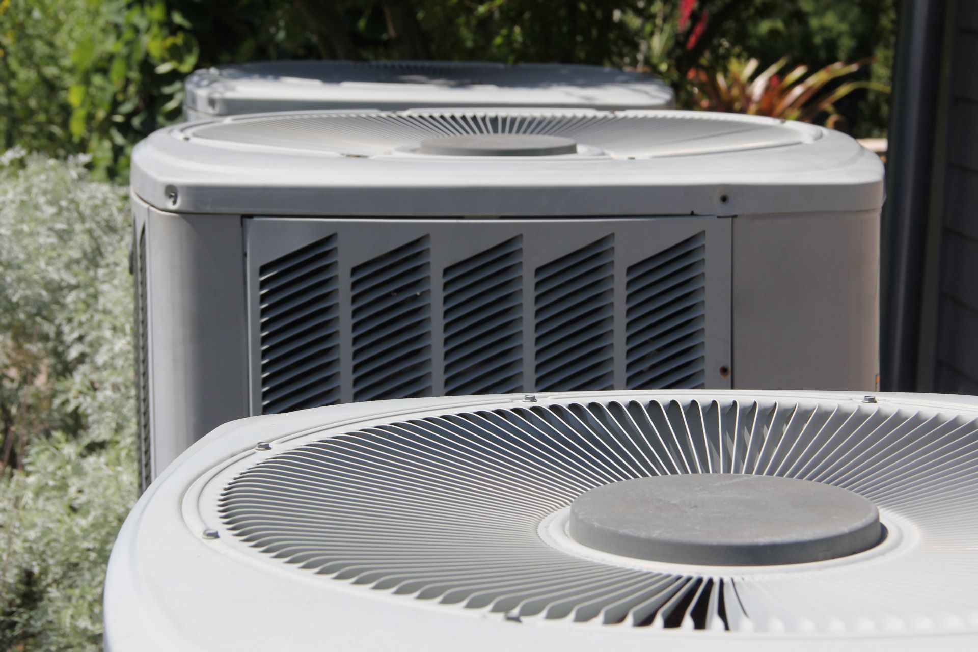 Two white outdoor air conditioning units in a landscaped yard