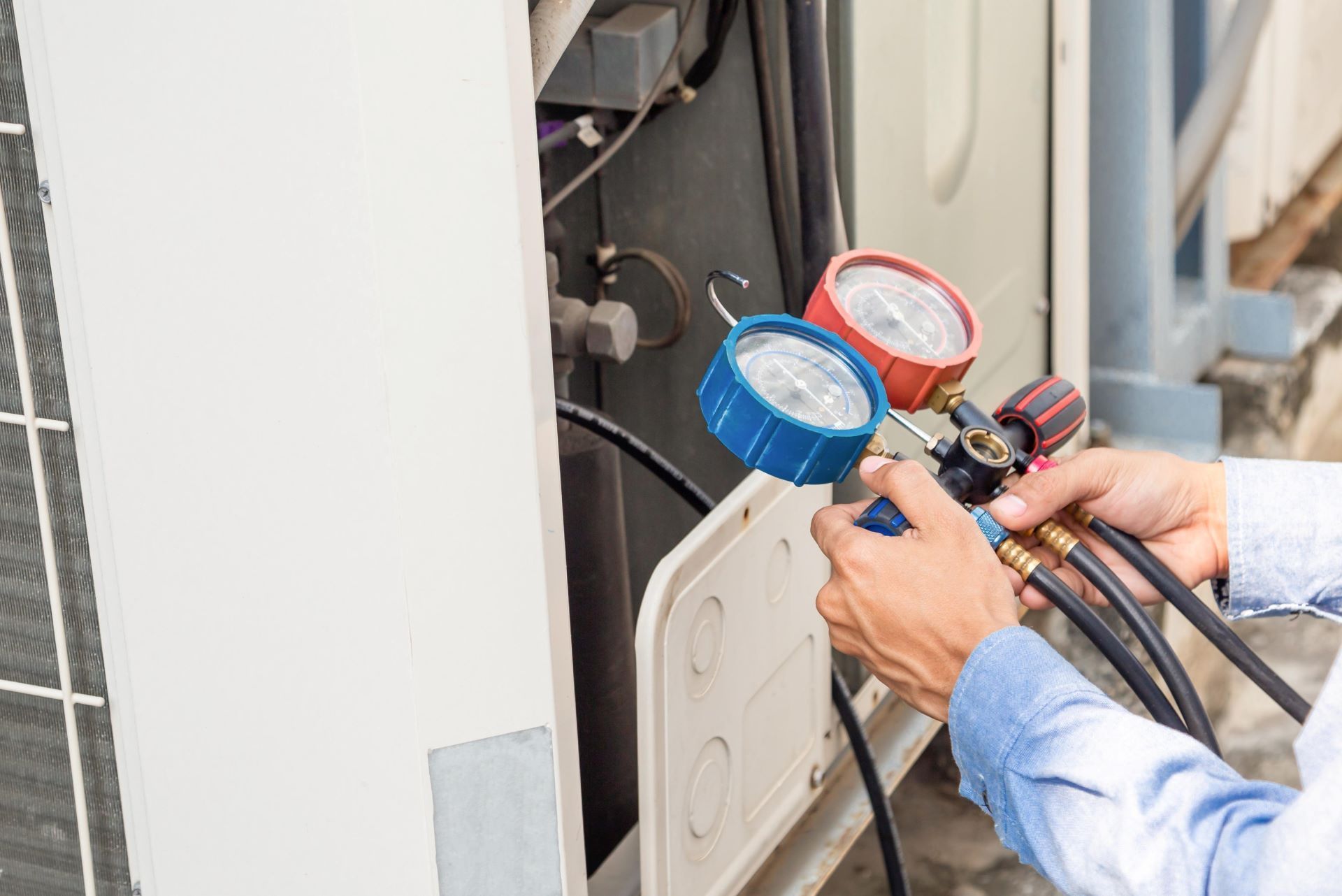 Technician using gauges and hoses to service an air conditioner unit outdoors