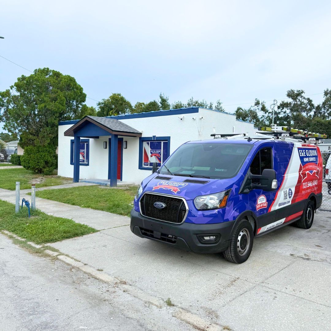 Branded blue delivery van parked beside a small white building on a residential street.