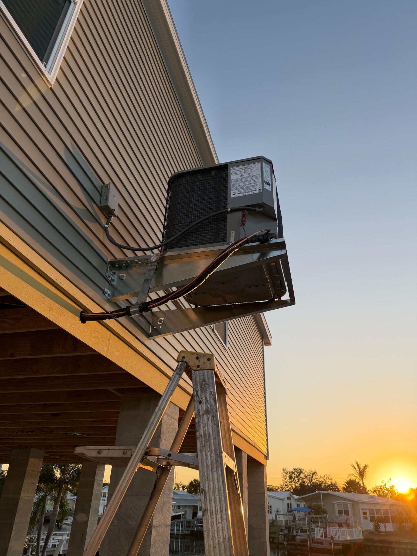 Crane lifting a large black unit beside a building at sunset