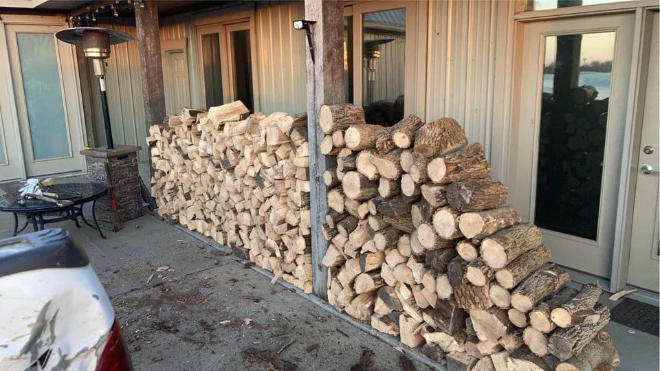 A large stack of firewood leaning against a building's wall on an outdoor porch.