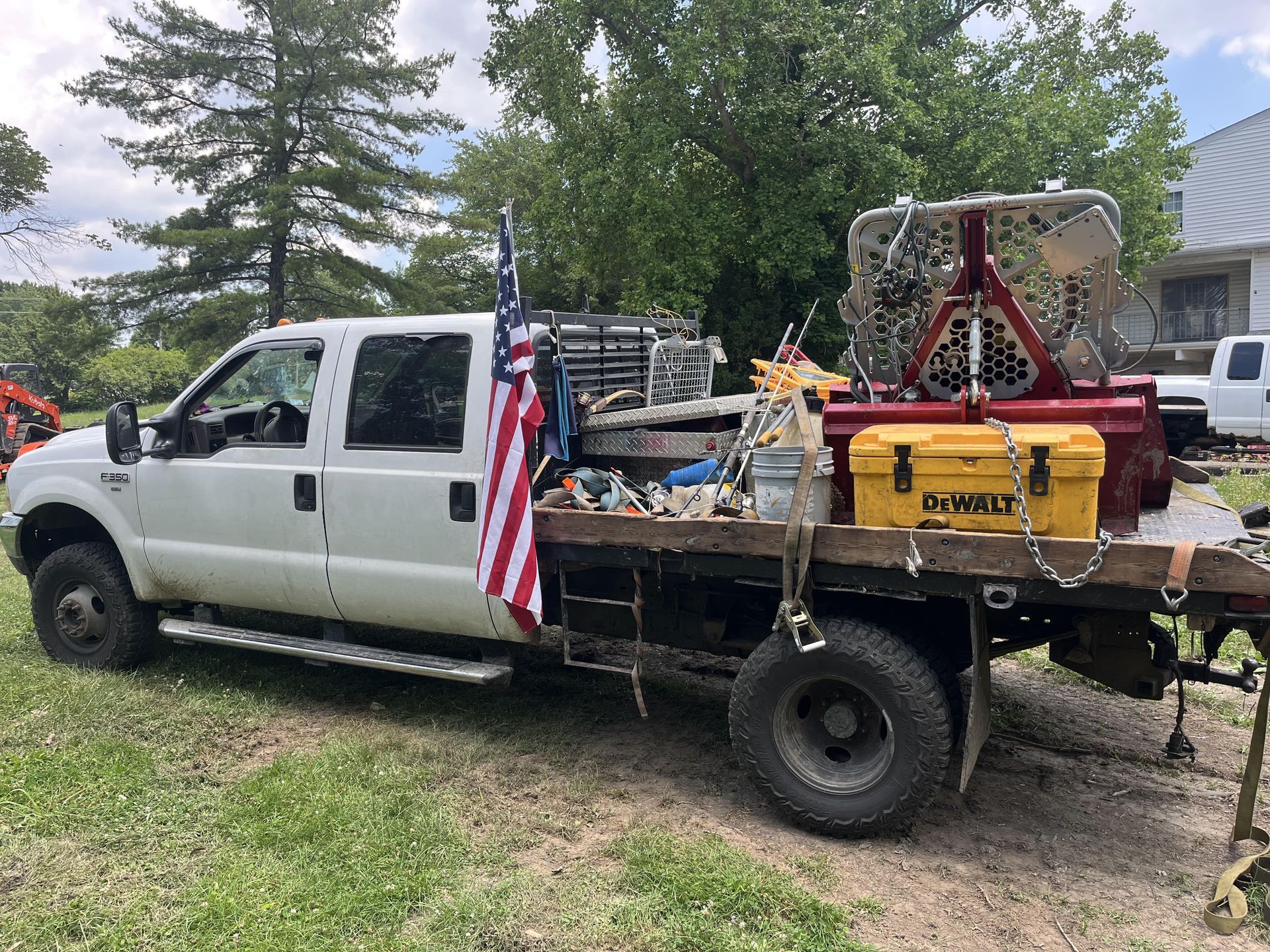 White truck with a flatbed carrying tools and equipment, American flag attached.