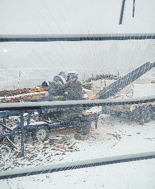 A tractor with an attached conveyor belt outside in the snow, next to a field.