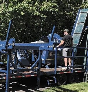 Man operating a blue wood chipper on a trailer, outdoors.