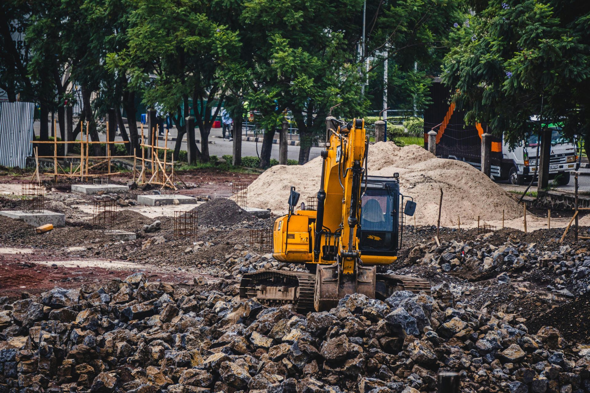 Yellow excavator on a construction site, surrounded by dirt, gravel, and trees.