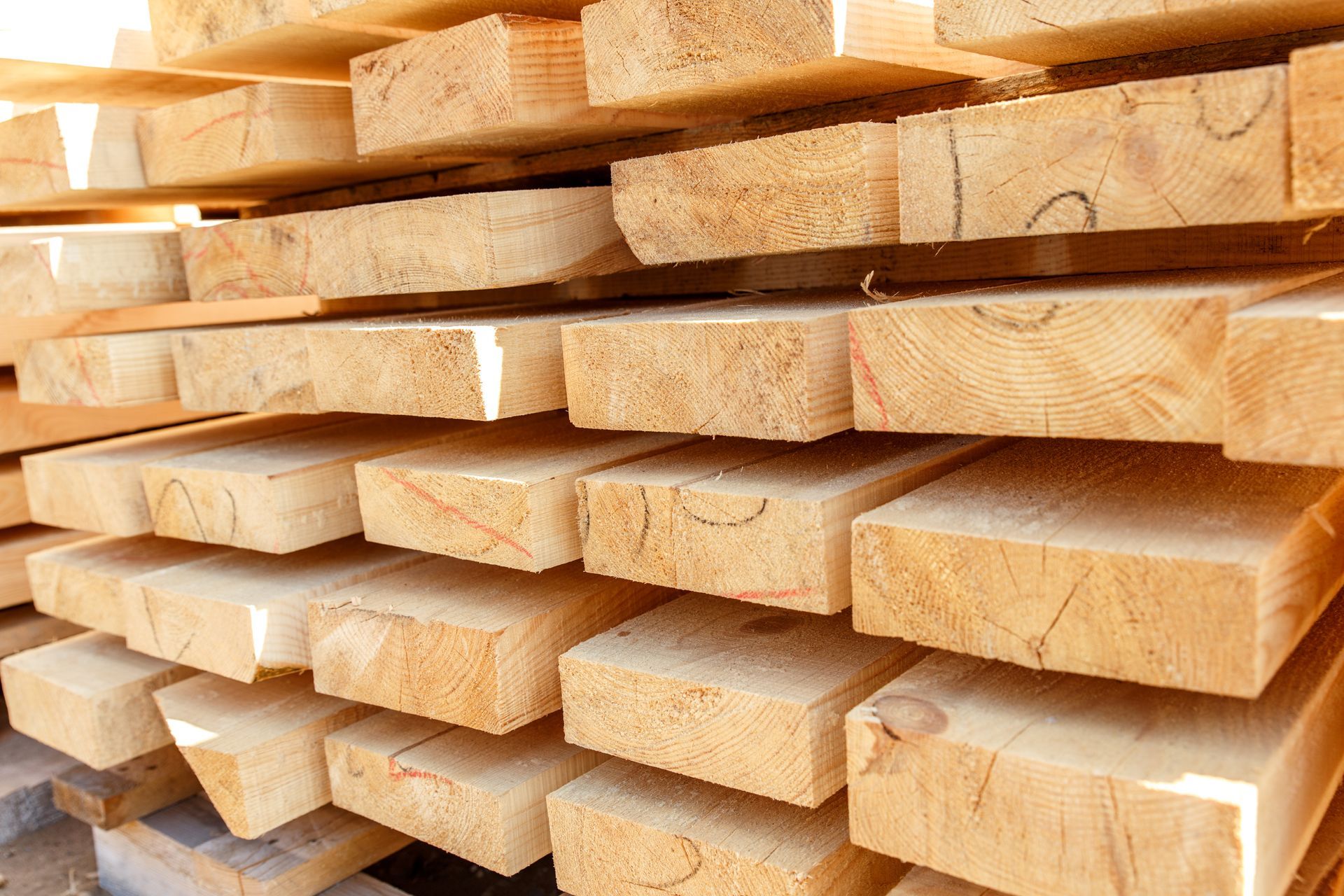 Stack of freshly cut wooden planks, light brown with visible grain, ready for construction.