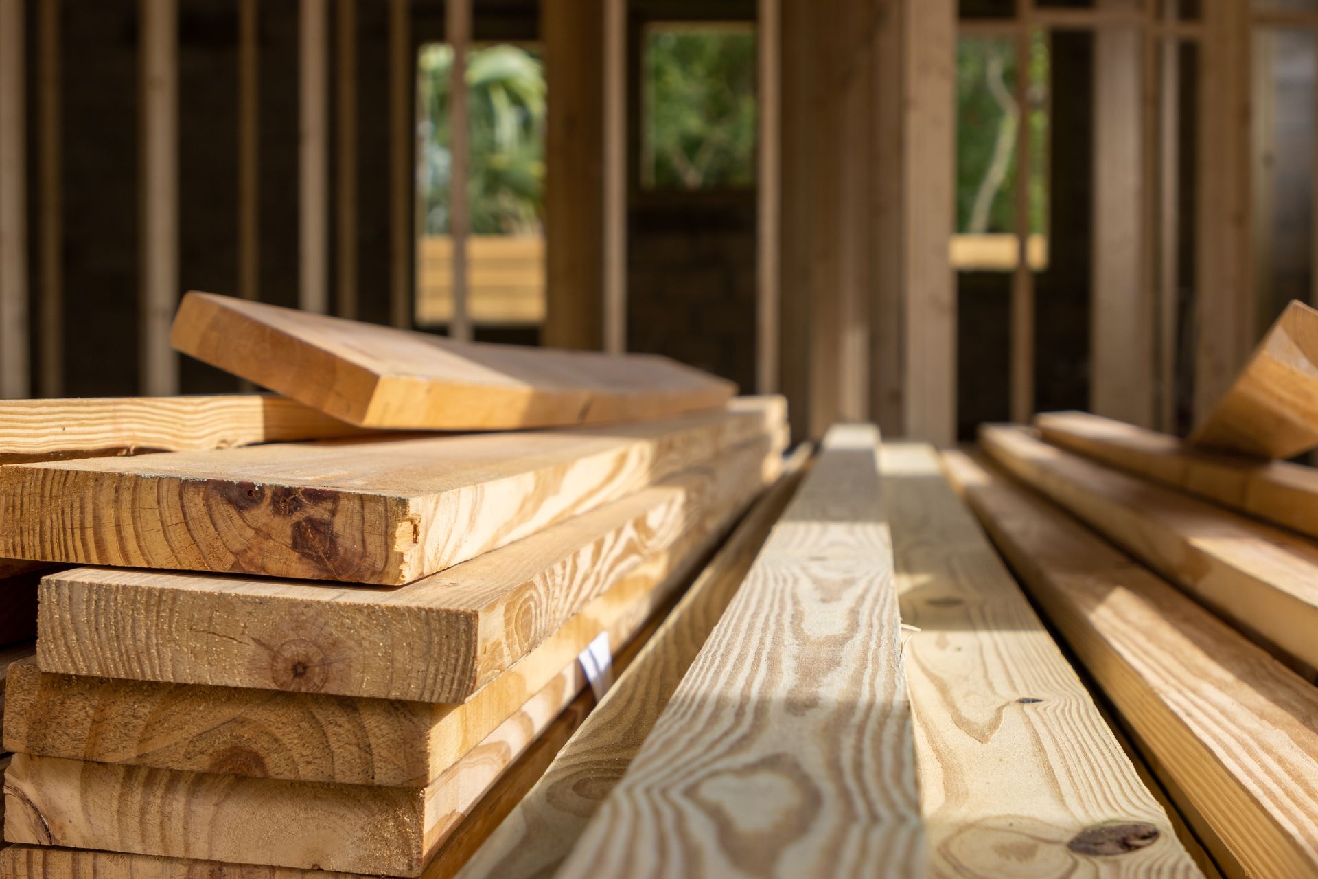 Pile of wood planks in a partially built wooden frame structure, bathed in sunlight.