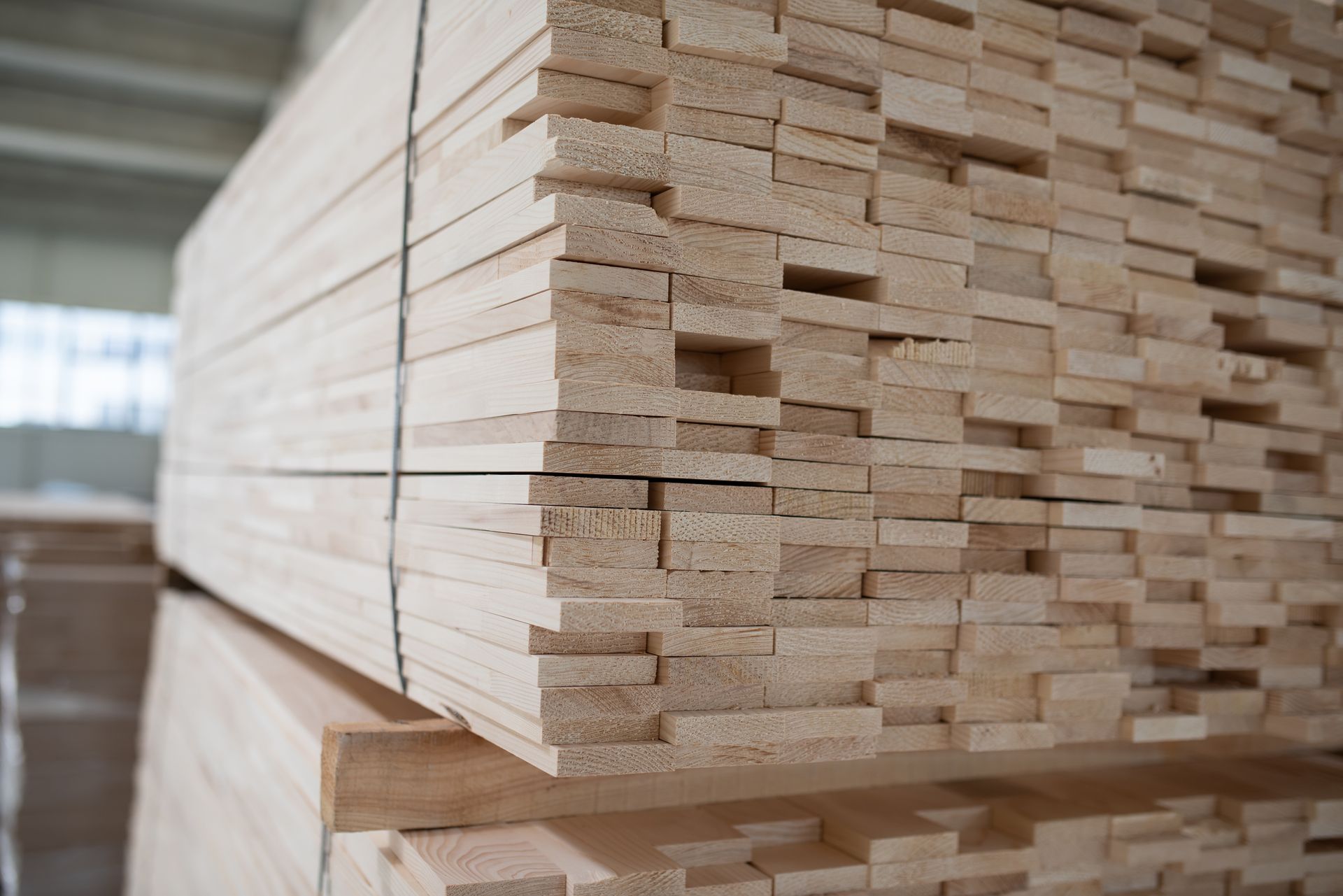 Stack of light-colored wooden boards bound together, likely for construction or carpentry, in a warehouse setting.
