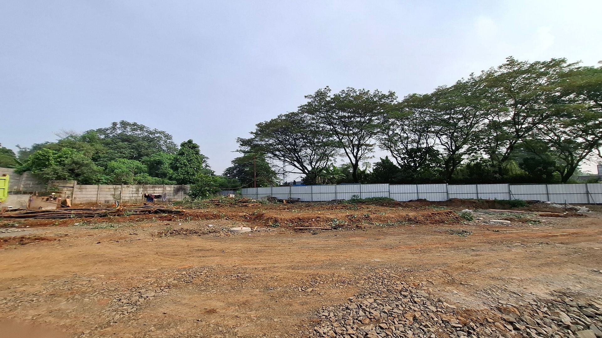 Cleared lot, brown soil, with a white and gray wall along the back, and trees along the top.