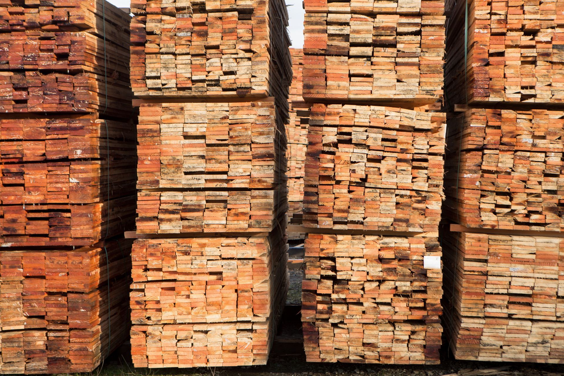 Stacks of reddish-brown lumber are neatly piled outdoors, ready for construction.