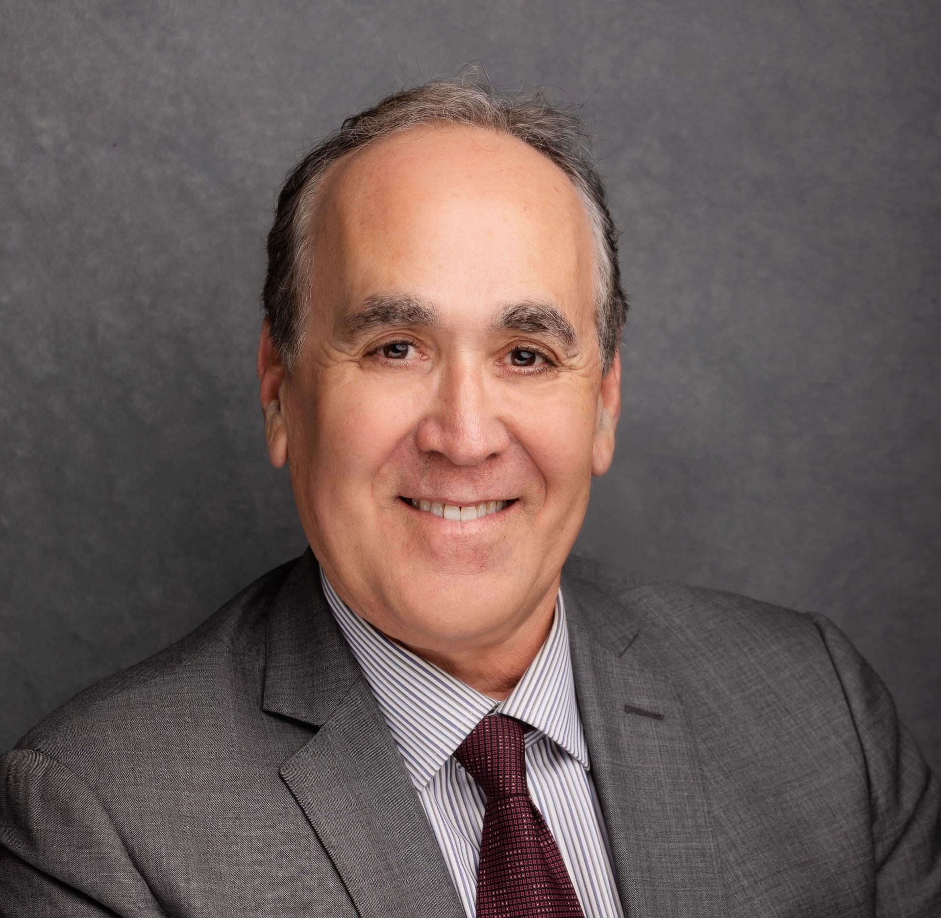 Smiling man in a suit and tie against a gray background.
