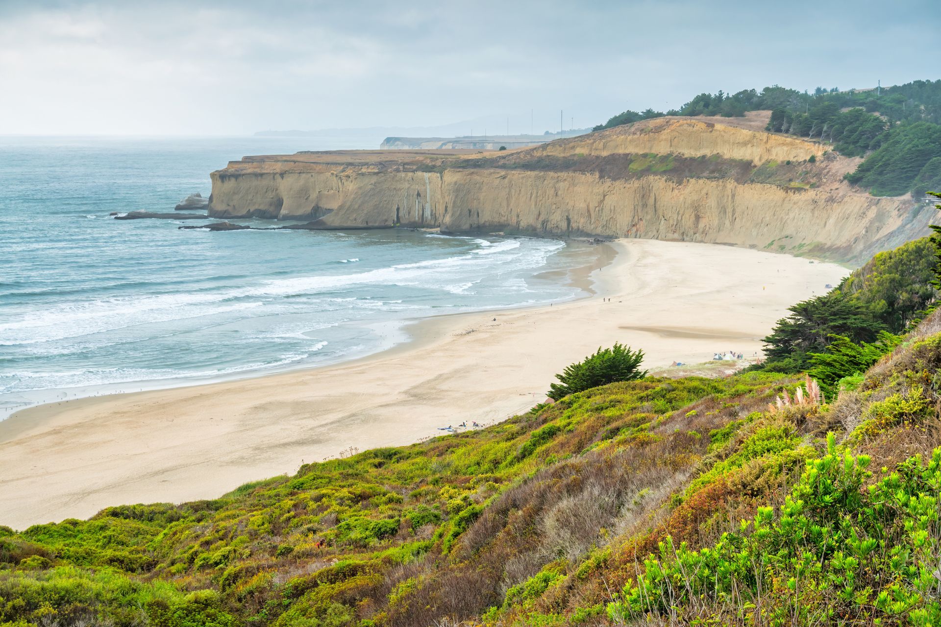 A view of a beach from a cliff overlooking the ocean.