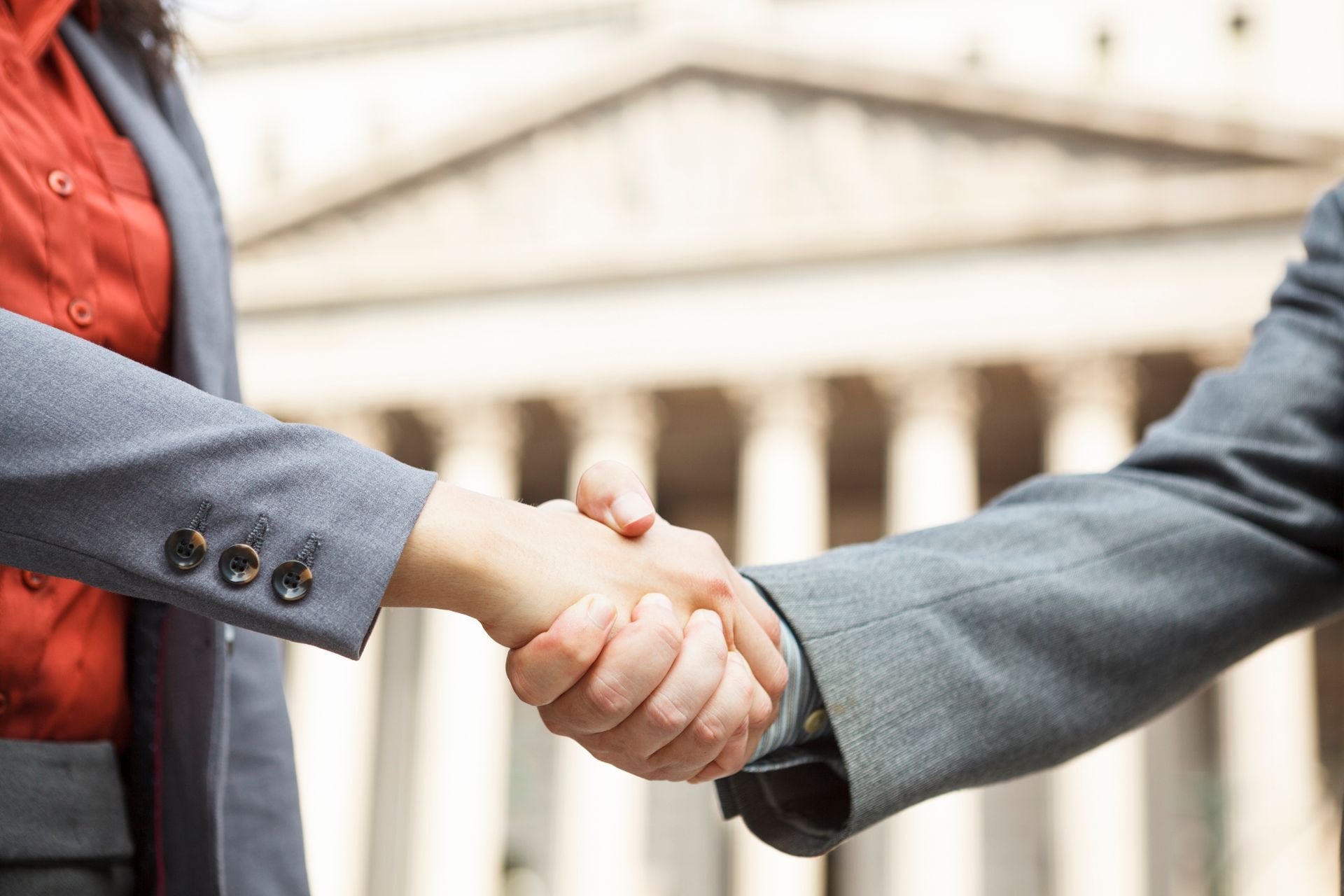 Two people are shaking hands in front of a building.