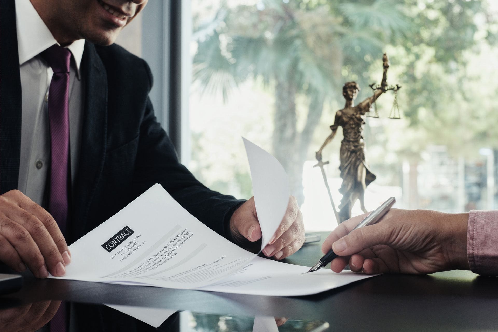 A man in a suit and tie is signing a document in front of a statue of justice.