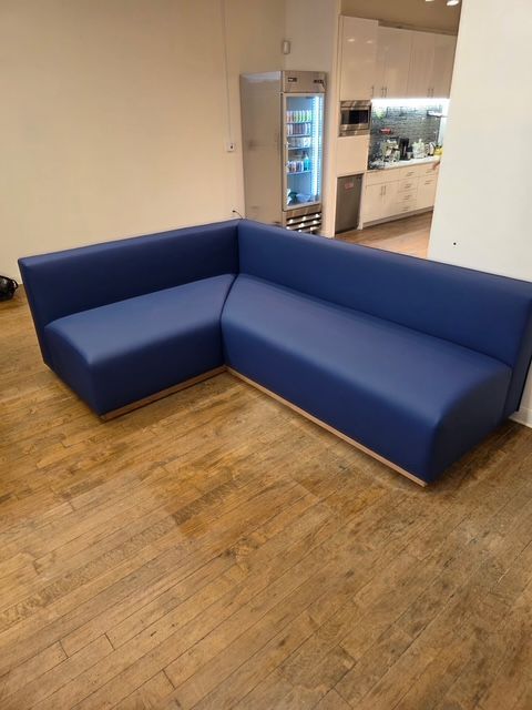 Blue L-shaped couch on a wood floor, near a white wall and kitchen area.