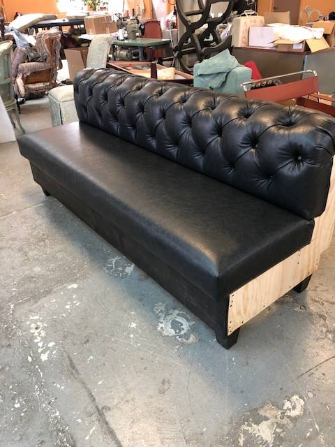 A black leather couch is sitting on a concrete floor