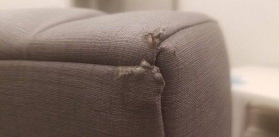 A close up of the corner of a couch with a hole in it.