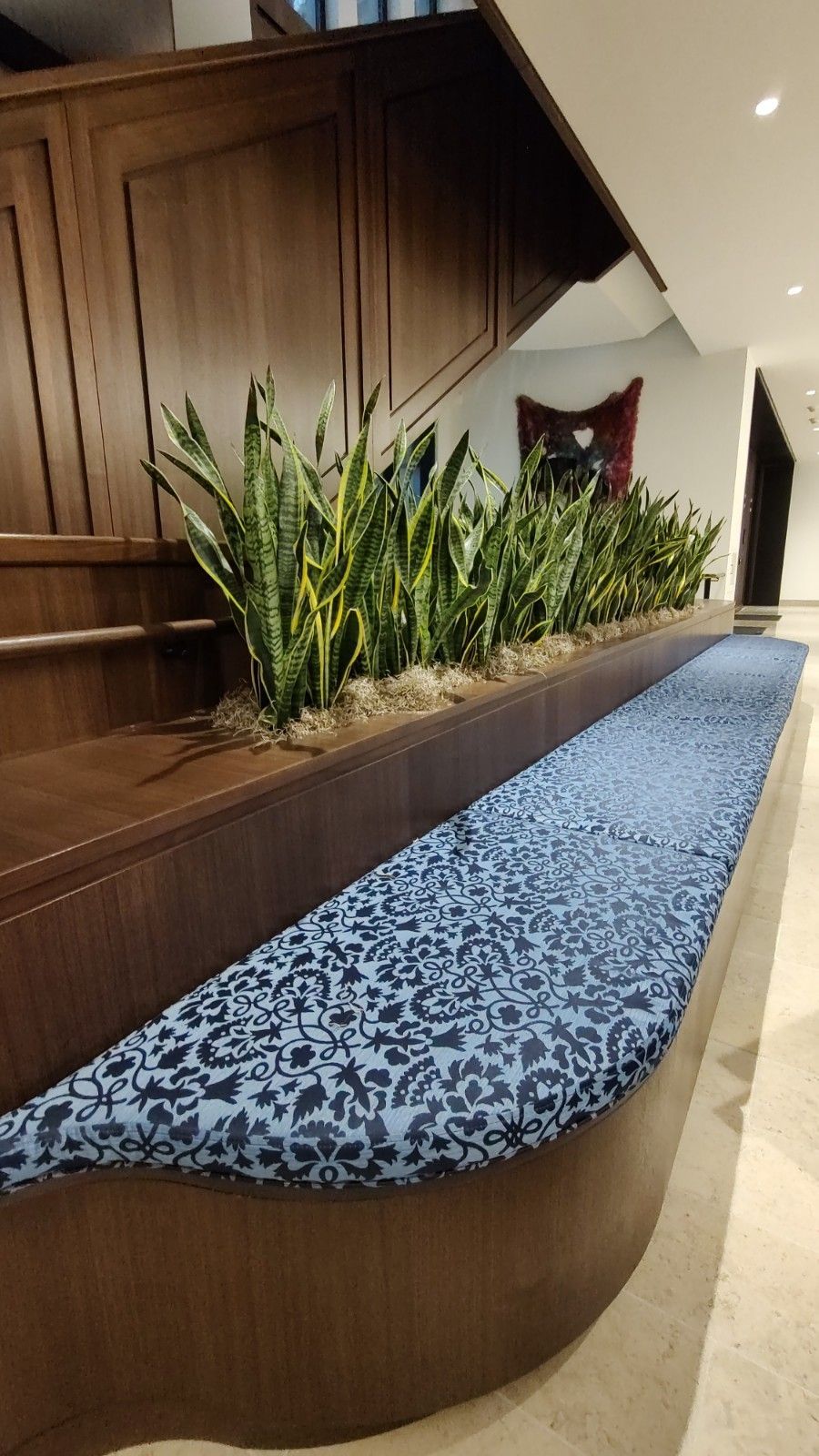 A wooden bench with a blue cushion and plants in it.