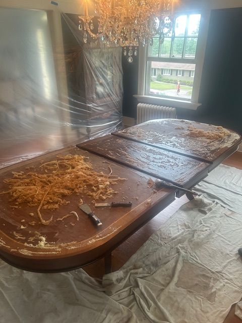 A dining room table is being painted in a room with a chandelier.