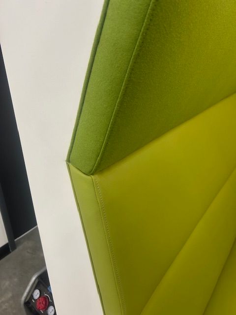 A close up of a green chair with a white wall behind it.