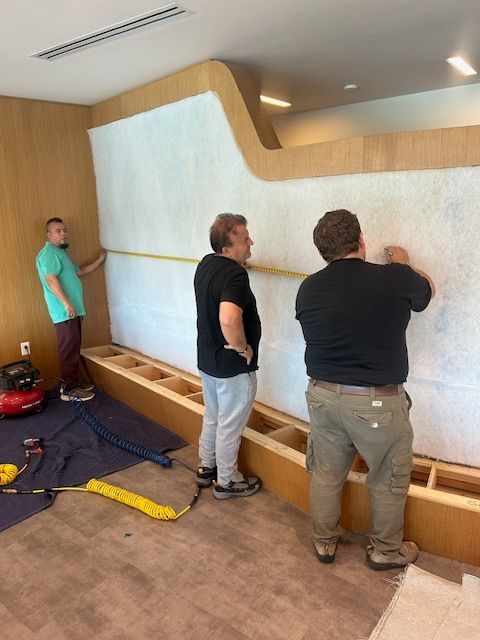 Three people measuring and working on a wall with insulation in a room.