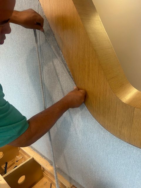 Person installs a light-colored wooden-framed, oval mirror on a light-gray wall.