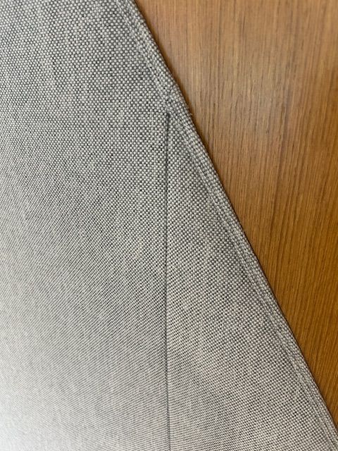 Close-up of gray fabric against a wooden surface, showing a seam and edge stitching.