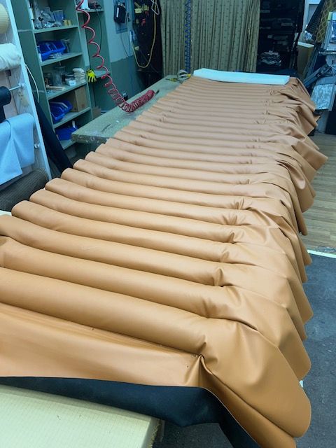 Tan pleated fabric stretched across a wooden table in a workshop setting.