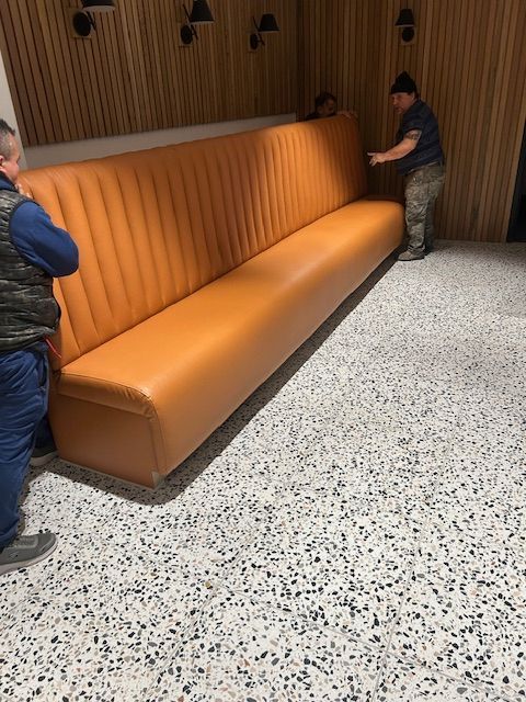 People move a long orange booth inside a room with a patterned floor and wood paneling.