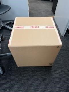 A cardboard box with fragile tape on it is sitting on the floor next to a chair.