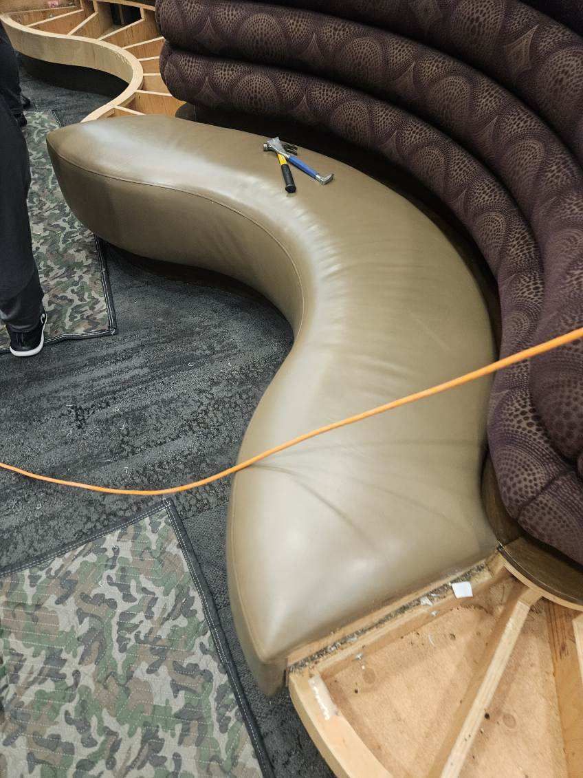 Curved beige leather sofa section next to a patterned brown sofa. An orange cord crosses the sofa.