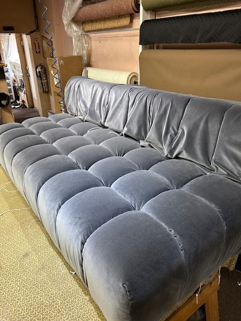 A grey couch is sitting in a room next to a stack of rolls of fabric.