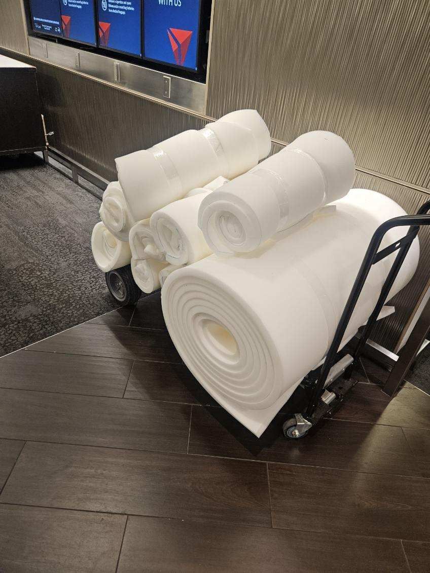 Cart loaded with large rolls of white material, likely fabric or paper, indoors near a screen.