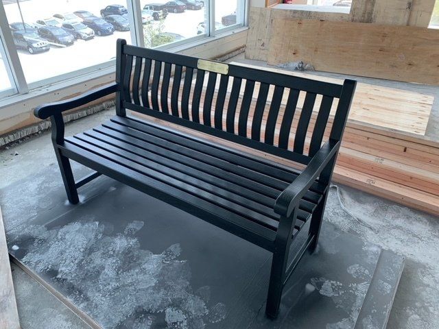 A black wooden bench is sitting in a room next to a window.