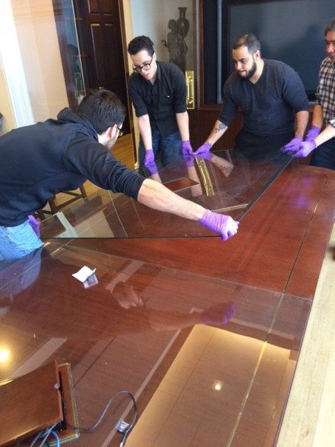 A group of men wearing purple gloves are working on a large wooden table