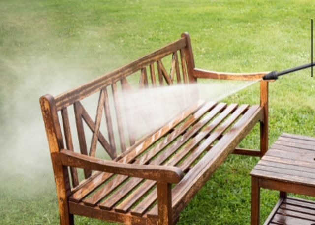 A wooden bench being pressure washed outdoors on green grass.