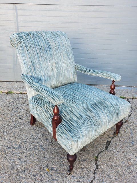 A blue chair is sitting on a sidewalk in front of a garage door.