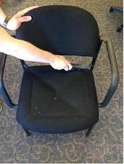 A person is holding the back of a black chair.