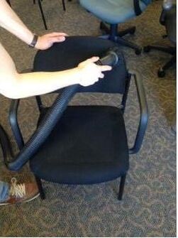 A person is cleaning a chair with a vacuum cleaner.