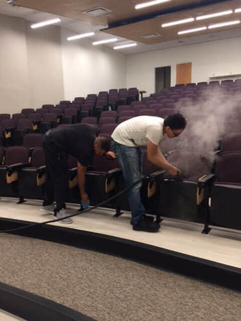 Two men are cleaning an auditorium with a vacuum cleaner